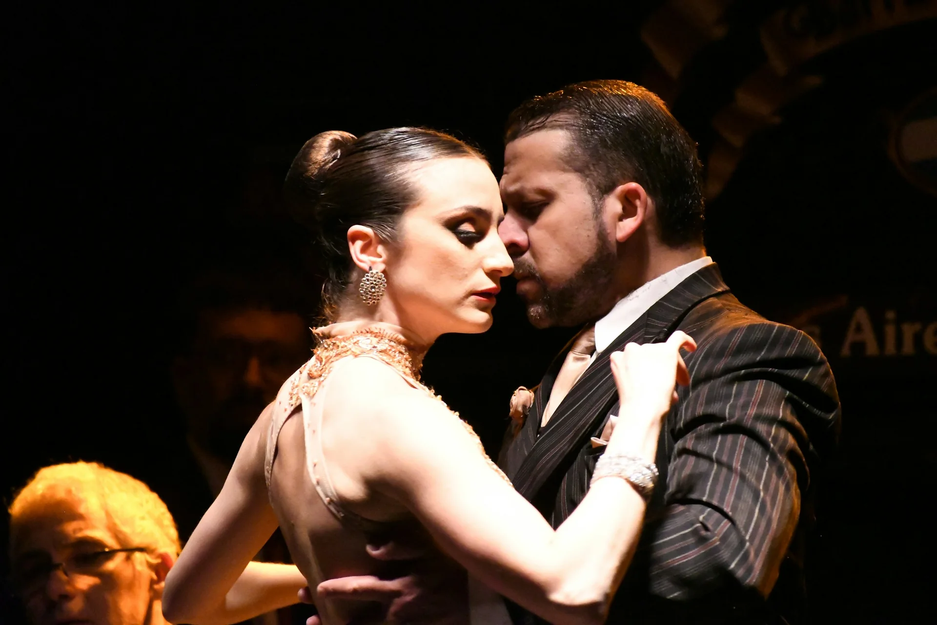 Tango pár tančící v těsném objetí pod teplým jevištním světlem, Buenos Aires