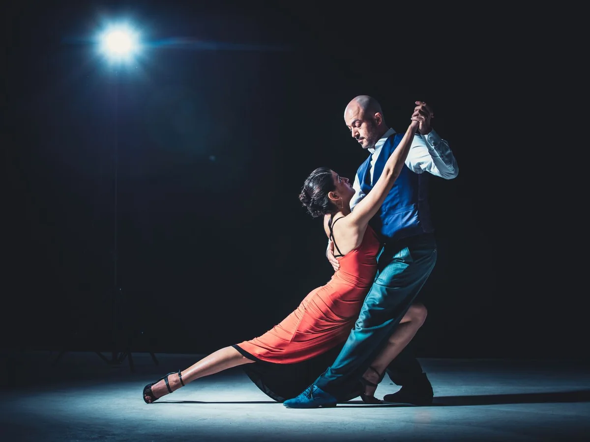 Tango pár v hlubokém záklonu pod jediným reflektorem na tmavém pozadí (reprezentativní fotografie)