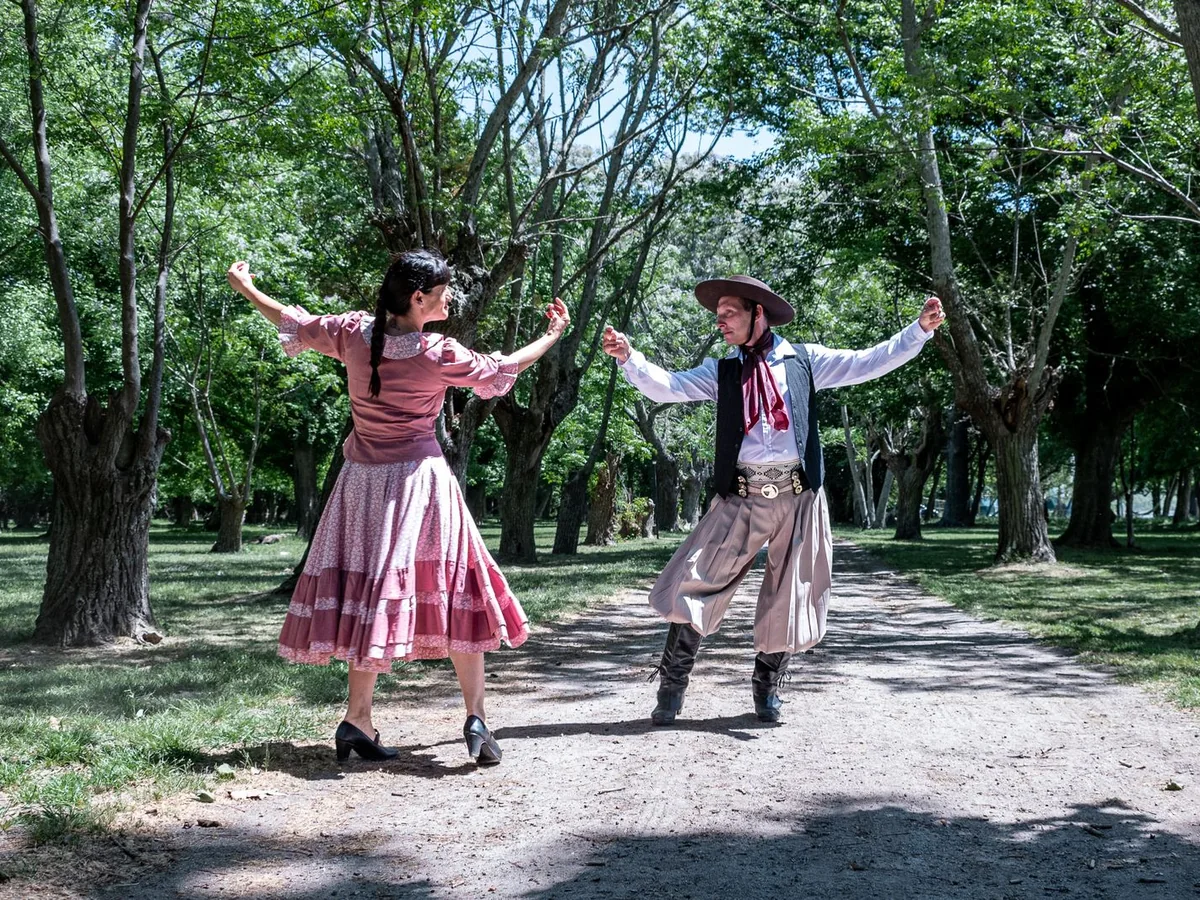 Pár v tradičním argentinském gaučovském a venkovském oděvu tančící pod širým nebem se zdviženýma rukama (reprezentativní fotografie)
